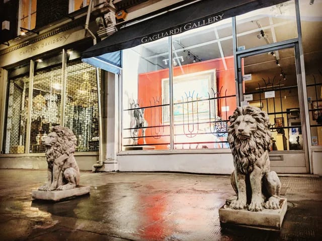 The Gagliardi Gallery shopfront on the King's Road at night, lit from within, the pavement wet and the pair of stone lions either side of the window