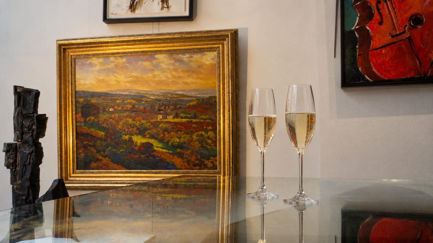 Two glasses of champagne on a glass table in the gallery, beside a Tuscan landscape in a gilt frame