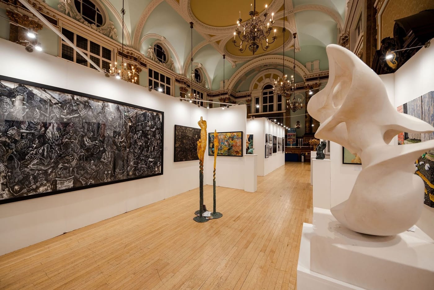 The London Art Biennale hung at Chelsea Old Town Hall, paintings along temporary walls under the hall's painted ceiling and chandeliers, with sculpture on plinths